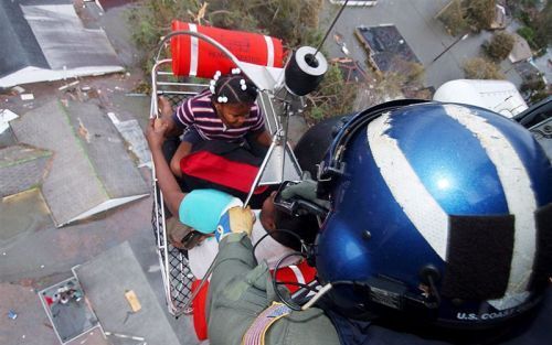 Kinderen worden aan boord van een kustwachthelikopter gehesen vanaf het dak van hun huis, terwijl hun ouders toekijken. - Foto EPA / Officer Kyle Miemi, Coast Guard