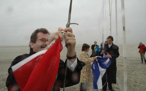 SCHIERMONNIKOOG - In de stromende regen haalt commissaris van de Koningin Alders de Groningse vlag neer op Schiermonnikoog. Op de achtergrond staat zijn ambtgenoot Nijpels gereed om de Friese PompeblÃªden te hijsen. - Foto RD