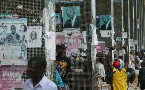 MONROVIA - Inwoners van Liberia lopen langs verkiezingsposters in de stad Monrovia. Voor het eerst sinds de veertien jaar durende burgeroorlog kunnen zij weer stemmen. Foto EPA.