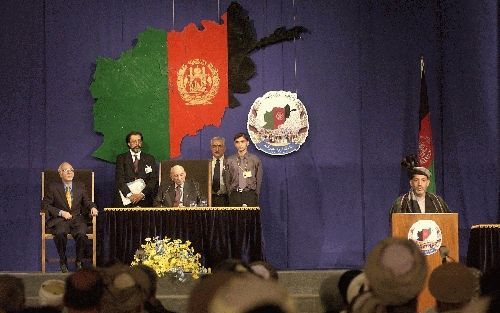 KABUL - Interim-premier Hamid Karzai sprak dinsdag bij de opening van de loya jirga in de Afghaanse hoofdstad Kabul de vergadering toe. Ex-koning Zahir Shah (zittend achter de tafel) luisterde toe. Woensdag reageerden loya jirga-leden boos op het feit dat