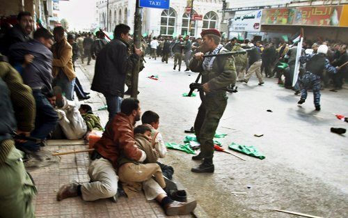 RAMALLAH – Een Palestijn probeert twee kinderen te beschermen, terwijl de oproerpolitie de betogende menige in bedwang tracht te houden. In Ramallah en Gaza braken vrijdag vuurgevechten uit tussen aanhangers van Hamas en Fatah. Het oplaaiende geweld doet 