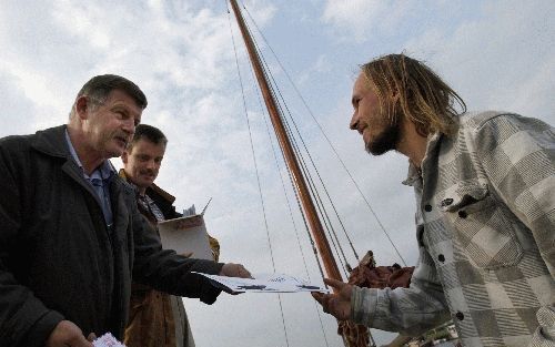 GENEMUIDEN - Voor de bootevangelisatiecommissie in Genemuiden is de zomer een drukke tijd. Op de foto overhandigen Klaas Booij (l.) en Tieme van Dijk (r.) aan een bootgast een envelop met christelijke lectuur van de kerken in Genemuiden. - Foto Dick(Vos