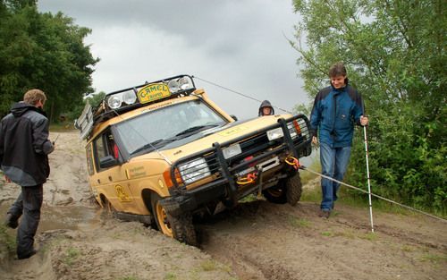 HILVARENBEEK – Een Land Rover rijdt zich vast in de modder. De bijna blinde Jan Bloem (r.) uit Apeldoorn inspecteert het ‘ongeval’ met de 4x4. Acht blinden en slechtzienden kropen maandag in Hilvarenbeek achter het stuur van een originele terreinwagen uit