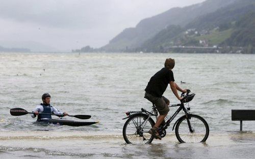 ZWITSERLAND - Niet alleen in Duitsland kampen mensen met wateroverlast. Ook in Zwitserland staan delen van het land onder water. Foto: Een fietser begroet een man in een kano aan de rand van een Zwitsers meer. Foto EPA