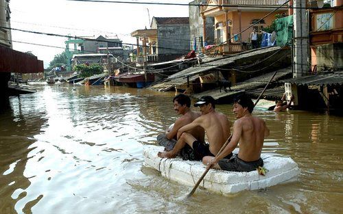 Mannen peddelen door ondergelopen straten in de provincie Thanh Hoa in Vietnam. Foto EPA