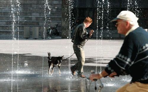 DEN HAAG - Wie zou het meest genieten? Een man loopt samen met zijn hond door de fontein van het Spui in Den Haag. De herfst is begonnen, maar het kwik steeg maandag op de laatste septemberdag tot boven de 20 graden. Volgens de weersverwachting blijft het