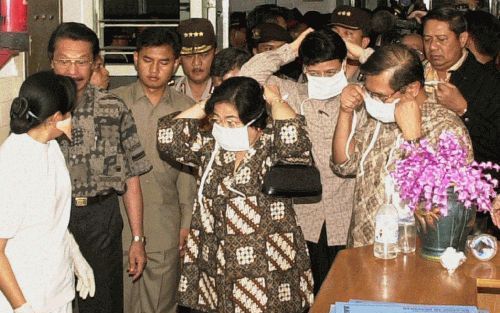 President Sukarnoputri en drie van haar ministers beschermen zich tegen stof en rook voordat ze de plaats des onheils bezoeken.Â¶ fotoverantwoording: Foto EPA