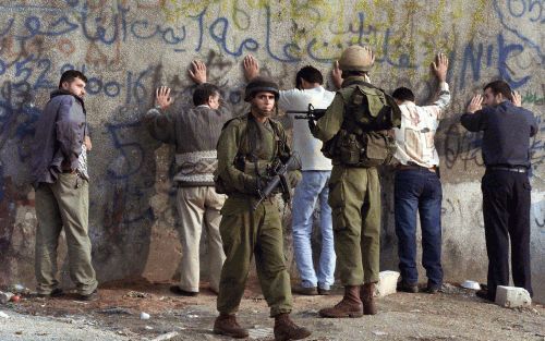 HEBRON - IsraÃ«lische militairen bewaken een groep Palestijnen die voor een routinecontrole in Hebron is aangehouden. - Foto EPA