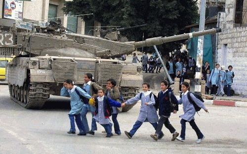 NABLUS - Palestijnse scholieren lopen langs een IsraÃ«lische tank die staat geparkeerd in Nablus op de Westelijke Jordaanoever. Het IsraÃ«lische leger heeft sinds juni de meeste steden op de Westelijke Jordaanoever weer bezet in een poging nieuwe Palestij