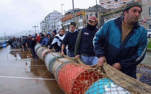 BAYONA - Spaanse vissers uit Bayona, in Noordwest-Spanje, slepen een visnet met olievaten naar het strand. Het gevaarte moet op zee voorkomen dat een nieuwe oliegolf de kust van Bayona bereikt. - Foto EPA