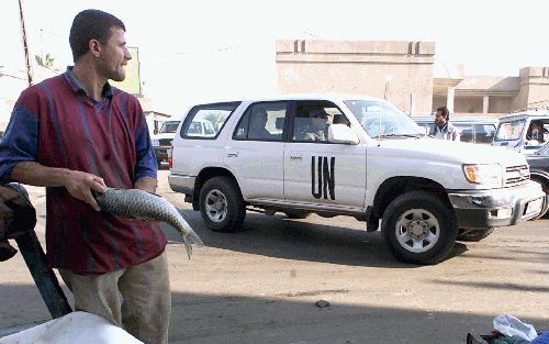 BAGDAD - Een Iraakse visverkoper kijkt naar passerende VN-wapeninspecteurs in Bagdad. De inspecteurs hebben Irak donderdag ervan beschuldigd dat het land onvoldoende aan de controles meewerkt. - Foto EPA