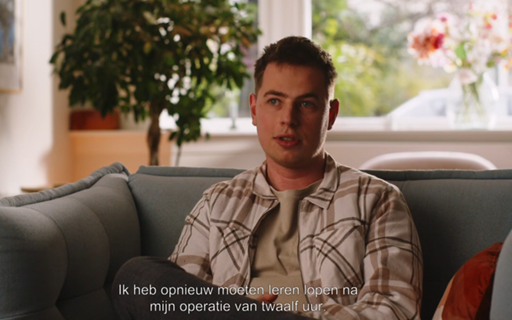 Een jongen in een geruite blouse zit op een bank. Achter hem een plant op stam.