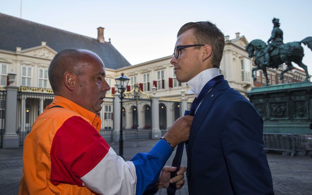 Vroege oranjefan Gerard van den Bosch uit Schiedam (L) helpt Ferry Floor uit Heerhugowaard met het strikken van zijn stropdas op Prinsjesdag bij paleis Noordeinde. ANP