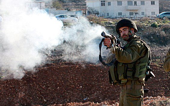 Een Israëlische militair schiet traangas tijdens een treffen met Palestijnse demonstranten. Israëlische grondtroepen zijn zondag verder de Gazastrook ingetrokken. Foto EPA