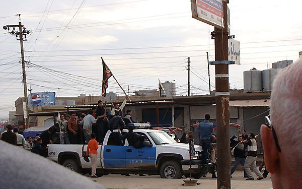 Shabakjongeren provoceren christenen in Bartalah met een islamitische vlag. Ze gebruiken daarbij een politieauto. Foto Jaco Klamer