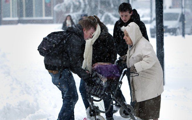 De 82-jarige mevrouw Knip uit Hoogezand heeft moeite om met haar rollator door de sneeuw te komen. Een groepje jongeren schiet te hulp. Foto ANP