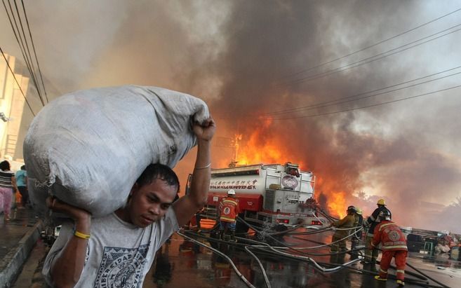 Een man vlucht met wat bezittingen uit de sloppenwijk Quezon. Foto EPA