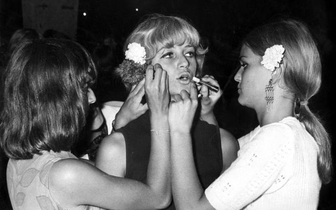 AMSTERDAM - Een hippiemeisje wordt door vriendinnen met lippenstift bijgewerkt, 11 augustus 1967. Volgens het economisch bureau van ING-onderdeel Postbank kopen vrouwen in economisch mindere tijden meer make-up. Foto ANP