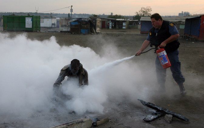 JOHANNESBURG - Een politieman blust een in brand gestoken slachtoffer van het geweld in Johannesburg. De man is met zware verwondingen opgenomen in het ziekenhuis. Foto EPA