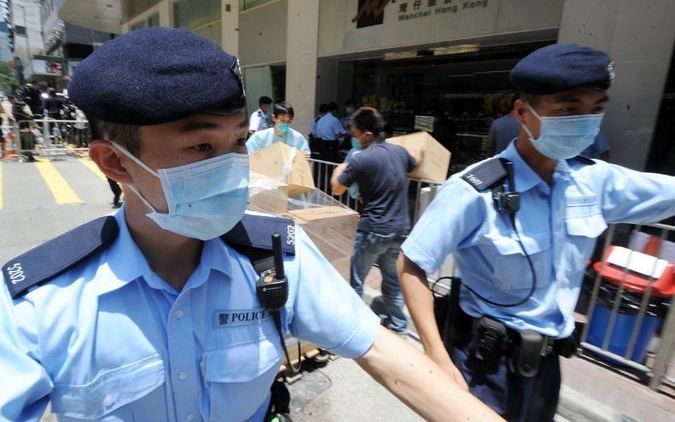 HONGKONG - Politieagenten met mondkapjes bewaken zaterdag de in- en uitgangen van het hotel Metropark in de wijk Wanchai, Hongkong. Foto ANP