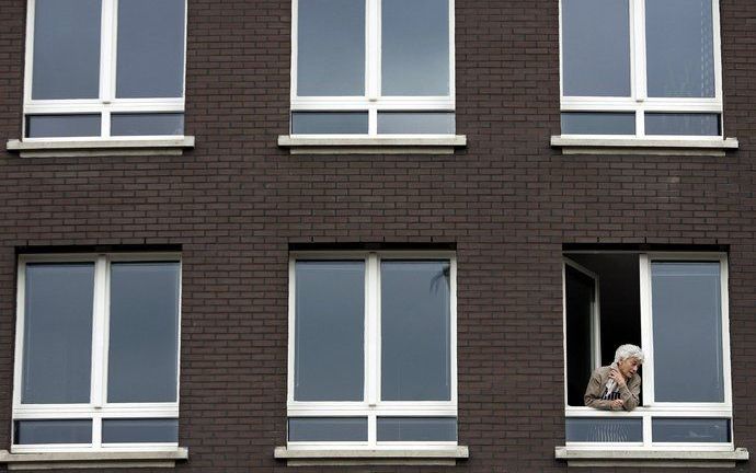 Komen de kinderen al? Een oudere vrouw kijkt uit het raam van haar appartement. Foto ANP