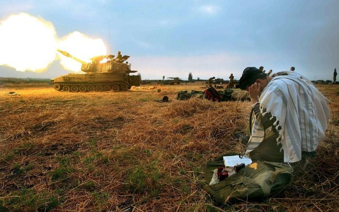 Een Israëlische militair bidt terwijl een tank een granaat afvuurt op Libanese doelen nabij de Israëlische stad Kiriyat Shmona, in juli 2006. Foto EPA