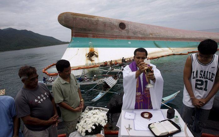 Een priester leidt een massabegrafenis voor het scheepswrak voor de kust van de Filipijnen. Foto's EPA