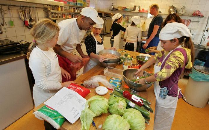 Onder begeleiding van een kok, een diëtiste en vrijwilliger Roberto werkt een kinderteam in het Amsterdamse Kinderkookkafé aan een Surinaams menu. De 9 jarige Nora (r.) knipt sperzieboontjes met een schaar. „Ik help mijn moeder ook elke dag bij het koken.