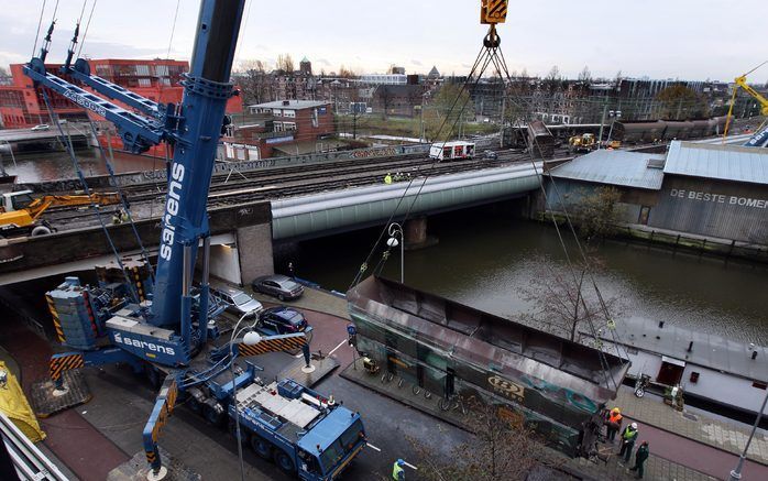 AMSTERDAM - Een van de wagons van de goederentrein die zaterdag in de buurt van het Centraal Station ontspoord is, hangt in de takels. Medewerkers van Prorail inventariseren de schade. Er rijdt geen of minder treinverkeer vanuit Amsterdam Centraal naar Am