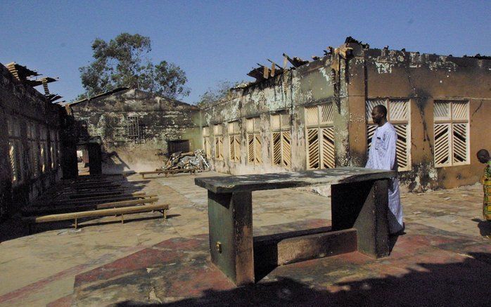 Een christen bekijkt zijn kerk, de Heilige Kruiskerk in de Noord-Nigeriaanse stad Kaduna, na een aanval door moslimmilitanten op 21 november 2002. De 78-jarige priester van de kerk, vader James Odion Iyere, werd zo zwaar mishandeld dat hij enkele dagen la