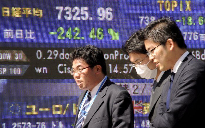 TOKIO - Japanse zakenlui lopen voor de borden met de zakkende koersen. Foto EPA