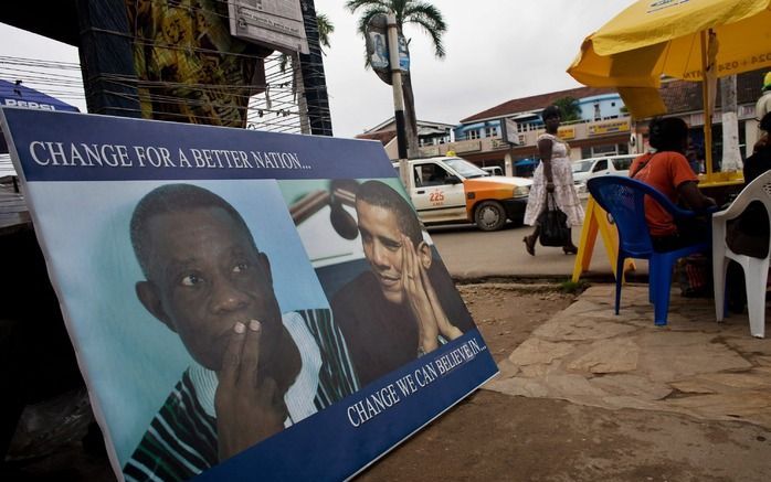 Ghanezen nuttigen hun lunch naast een reclamebord met de foto's van de Ghanese president John Atta Mills en de Amerikaanse president Barack Obama. Het gezin Obama kwam vrijdagavond aan in het Afrikaanse land. Foto EPA