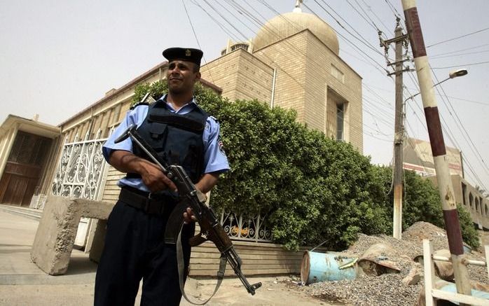 BAGDAD – Een Iraakse politieagent maandag bij de ingang van een kerk in de Palestijnenstraat in Bagdad, waar een dag eerder een aanslag met een bomauto was gepleegd. Een golf van aanslagen teistert in Irak de christelijke kerken. Foto EPA