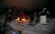 Palestijnen rond een vuurtje in hun verwoeste huis in de Gazastrook. Foto EPA