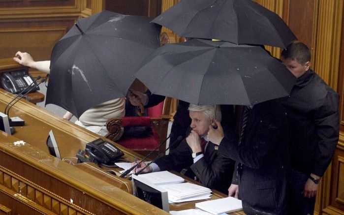 De Oekaïnse parlementsvoorzitter moest zich dinsdag verschuilen achter paraplu’s omdat hij werd bekogeld met eieren. Foto EPA