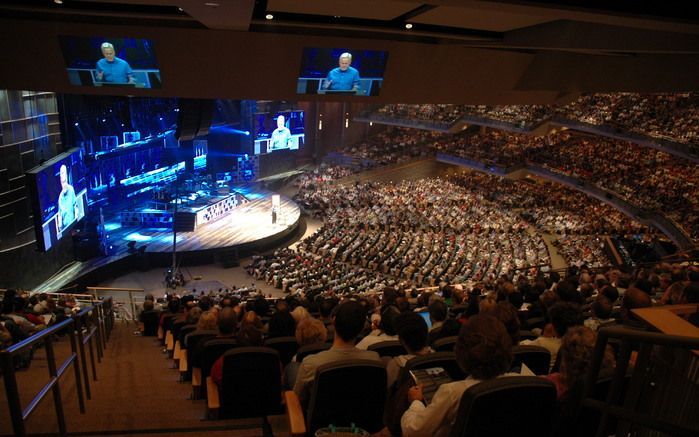 Een leiderschapsconferentie (summit) in het –7200 zitplaatsen tellende– auditorium van de Willow Creek Community Church (WCCC) in Chicago. Op het podium, en geprojecteerd op vier grote schermen, WCCC hoofdvoorganger Bill Hybels. Conferenties als deze word