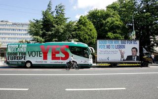 DUBLIN - Een fietser in de Ierse hoofdstad Dublin passeert twee bussen die zowel oproepen 'JA' als ´NEE´ te zeggen tegen het Europese referendum, dat vandaag in Ierland wordt gehouden. - Foto EPA