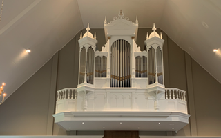 Foto van een orgel met een witte kas, op een galerij.