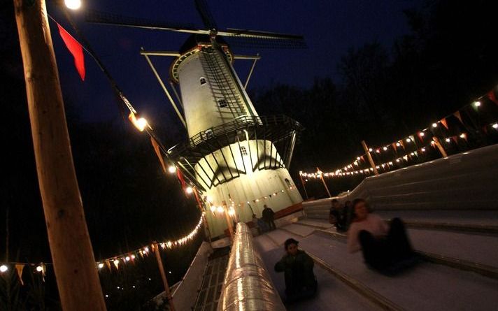 Winter in het Openluchtmuseum. De koude avond is gevallen. Tonnen met brandend hout verlichten en verwarmen de bezoekers. De sleebaan bij de molen is misschien nog wel populairder dan de ijsbaan. Allemaal nep, maar wat geeft dat. Foto’s VidiPhoto