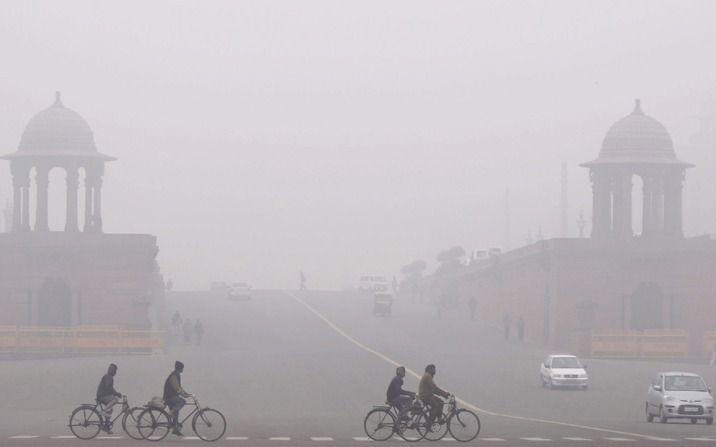 Fietsers rijden door de dichte mist in de Indiase hoofdstad New Delhi. Foto ANP