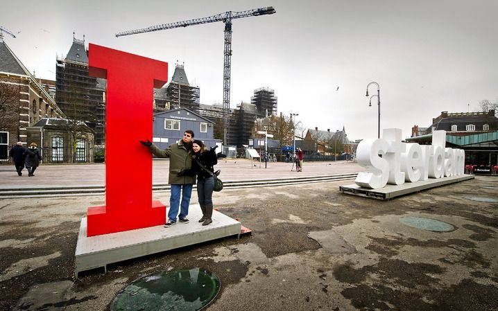 Twee toeristen poseren dinsdag voor het I AMsterdam logo op het Museumplein in Amsterdam. De letters A en M uit het logo waren dinsdagochtend verdwenen. Inmiddels zijn ze teruggevonden. Foto ANP