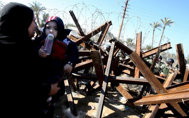 RAFAH - Een Palestijnse vrouw met haar kind bij de grens tussen de Gazastrook en Egypte. De gesloten Rafah–grensovergang gaat mogelijk weer open nu Israël akkoord gaat met een bestand met de Hamas–beweging. Foto EPA