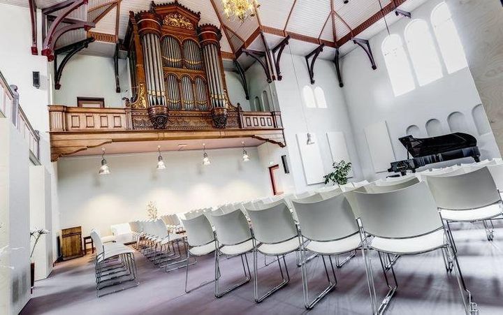 Een lichte zaal, met een kerkorgel, een vleugel en witte stoelen.
