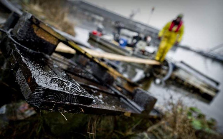 Een met olie besmeurde pallet ligt aan de kade terwijl op de achtergrond iemand bezig is met wegpompen van de olie. Foto ANP