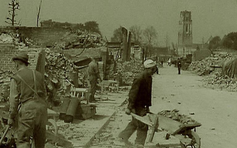 Onder regie van de Duitsers zijn arbeiders in Rotterdam al snel bezig met kruiwagen de puinhopen op te ruimen na het Duitse bombardement, mei 1940. Op de achtergrond de toren van de Laurenskerk. beeld Bundesarchiv/DIG IT UP