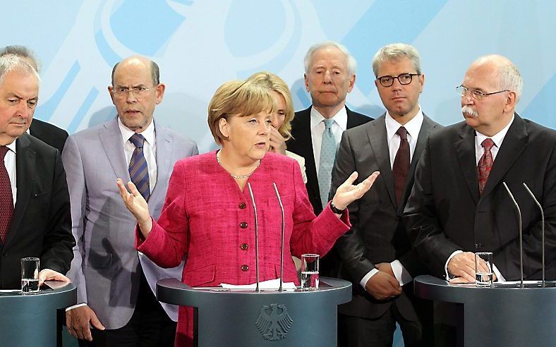 Merkel (m.) ligt het regeringsbesluit toe. Foto EPA