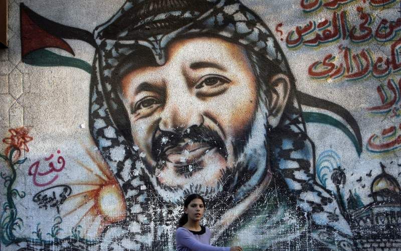 Een meisje passeert in Gaza-stad een muur waarop een reusachtig portret is geplakt van de voormalige Palestijnse leider Jasser Arafat. Foto EPA