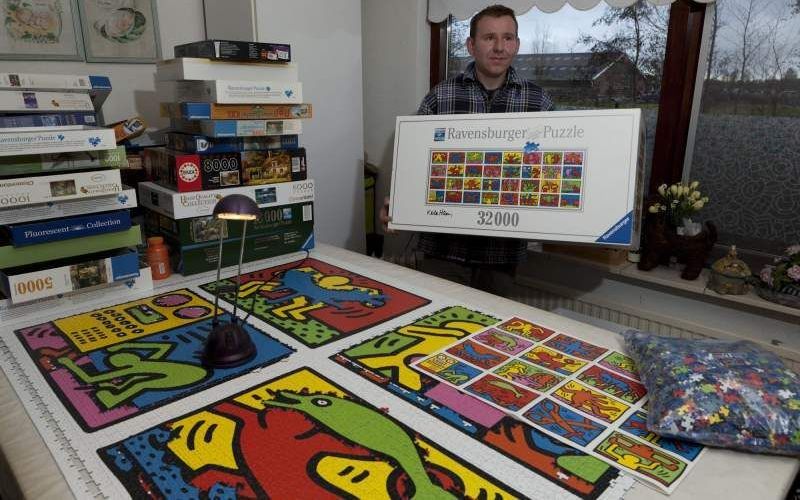 Jean-Paul Klostermann uit Ouderkerk aan den IJssel maakt een puzzel van 32.256 stukjes. Op tafel ligt het eerste deel van de puzzel, die uiteindelijk 5,44 bij 1,92 meter groot moet worden. Rechts een van de acht zakken puzzelstukjes. Foto André Dorst