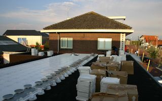 Isolatiemateriaal op een plat dak. Daarachter zijn de ramen en het puntdak van een woning zichtbaar.