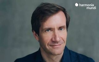 Een man van middelbare leeftijd met een donker overhemd aan kijkt recht de camera in.